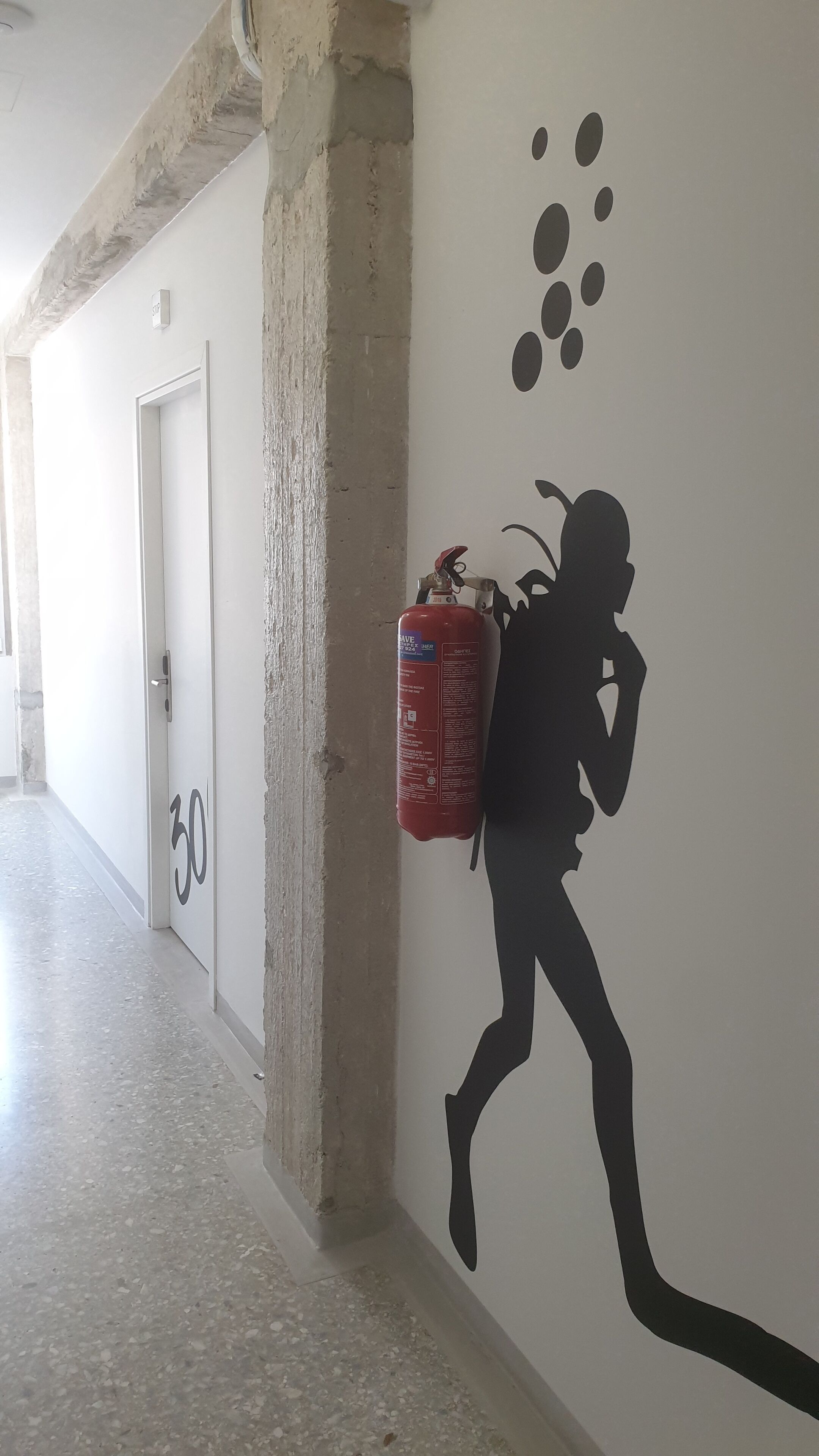 Un corridoio con un estintore fissato al muro, una porta con la scritta '30' e il numero '30' sul pavimento.