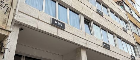 Un edificio de varios pisos con estilo arquitectónico moderno, que cuenta con amplios ventanales, señalización para distintos negocios y una entrada visible.