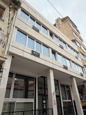 A multi-story building with a modern architectural style, featuring large windows, signage for different businesses, and a visible entrance. - athensdot (Athens)