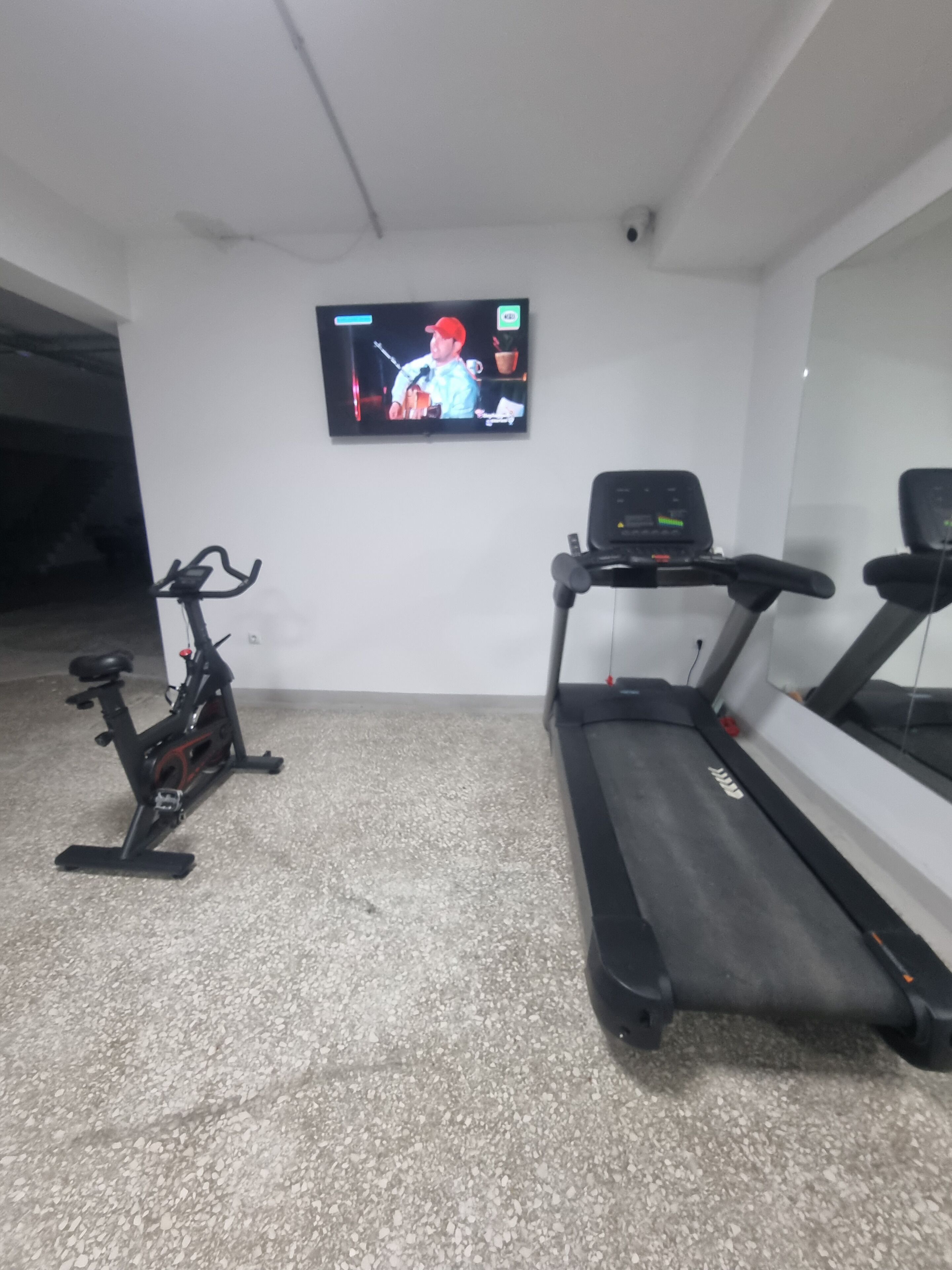 Un gimnasio con cinta de correr, bicicleta estática y una televisión en la pared.
