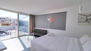 Una habitación de hotel moderna con una cama grande, un sofá, una mesita y un balcón con vistas a la ciudad.
