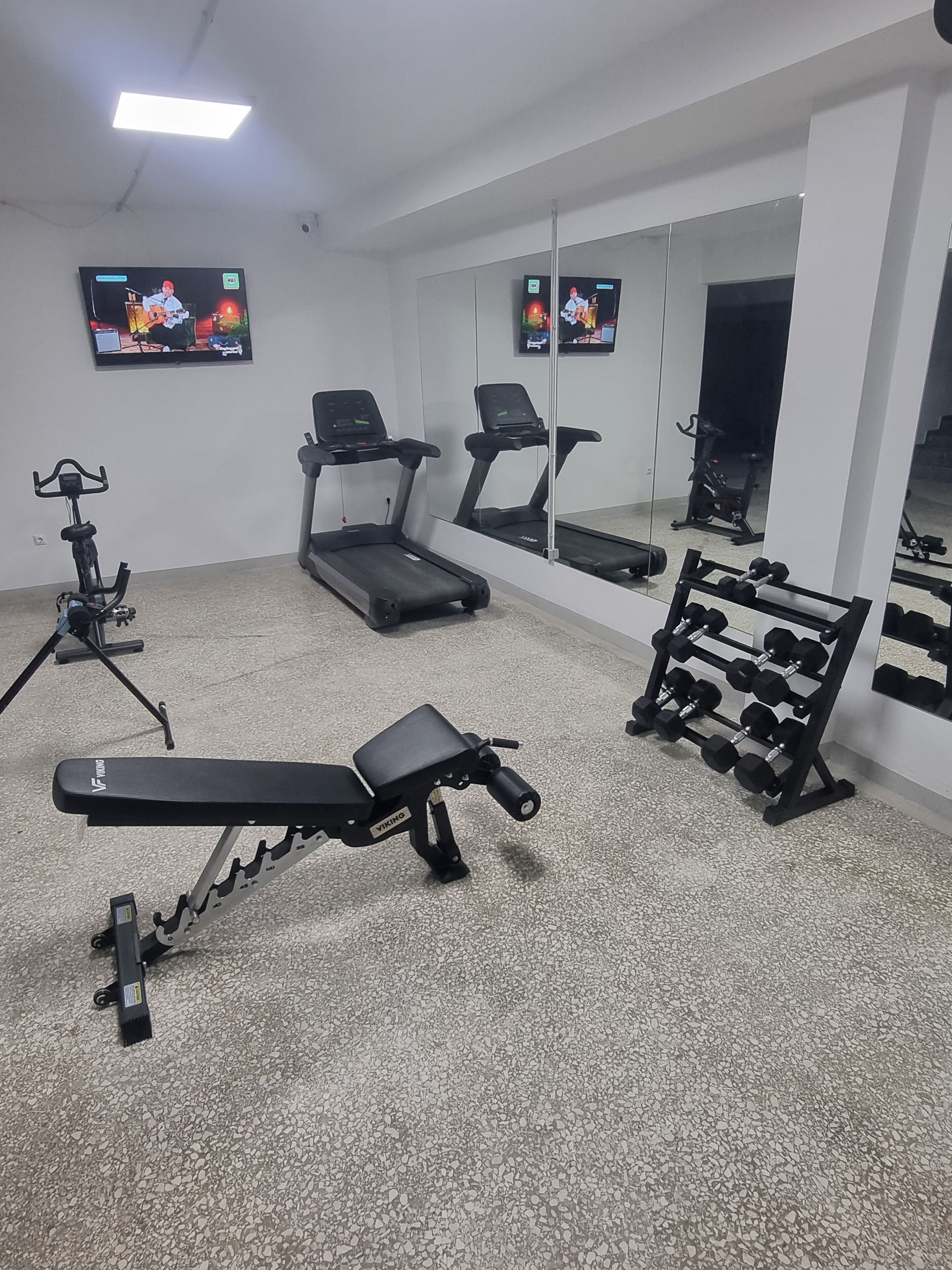 A gym with exercise equipment including a treadmill, stationary bike, bench press, and dumbbells.