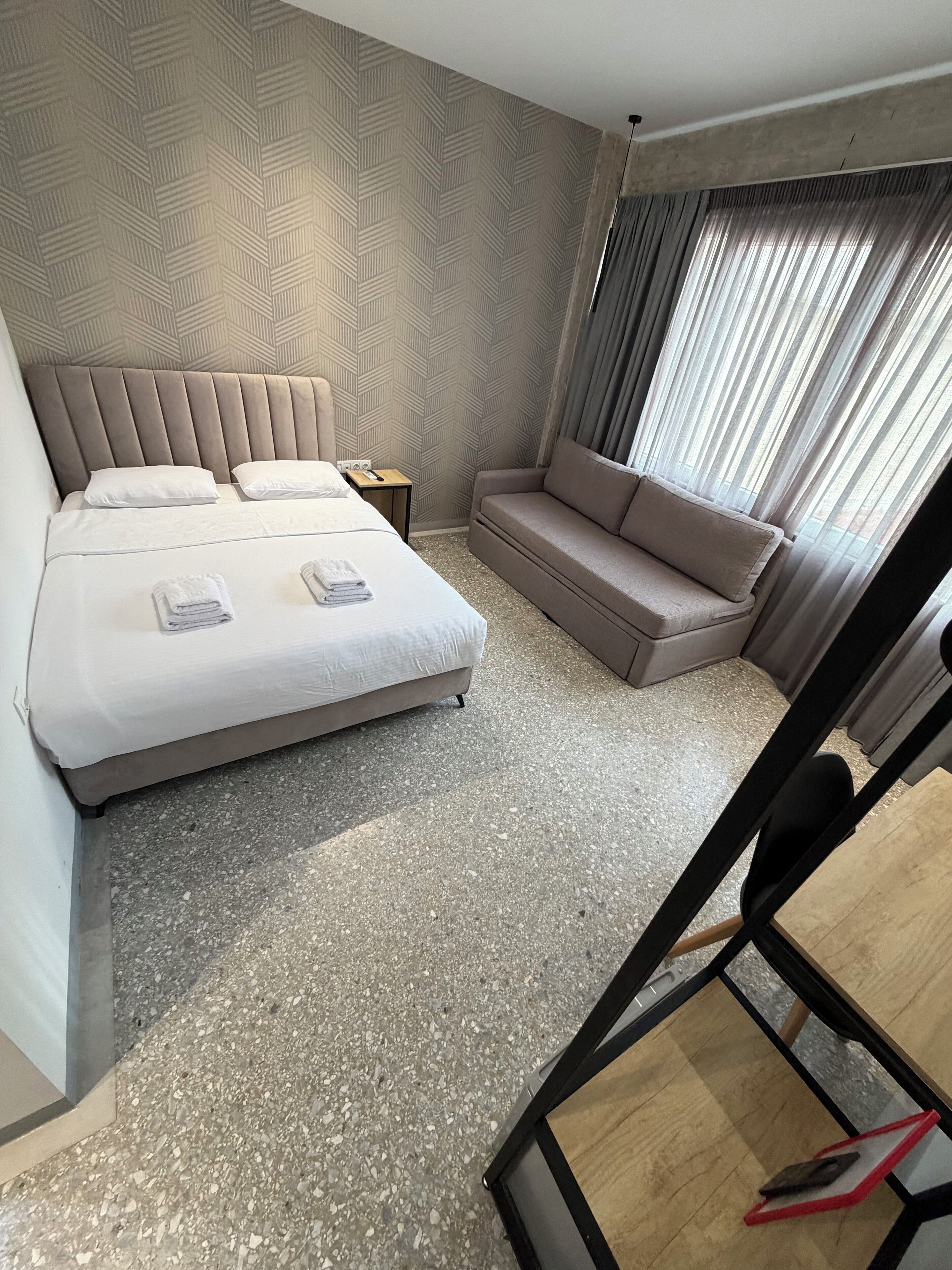 Una habitación de hotel con una cama, un sofá, una mesita y una ventana con cortinas.