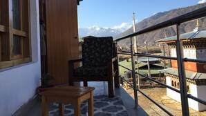 Ein Balkon mit Stuhl und Tisch, Blick auf Berge und traditionelle Architektur im Hintergrund.