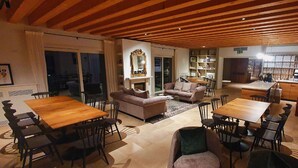 Een ruime woonkamer met een houten plafond, een open haard en een eethoek met een grote tafel en stoelen.