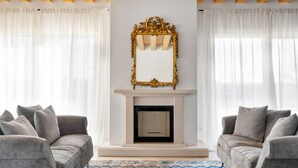 Een woonkamer met een open haard, twee grijze banken en een grote spiegel met een decoratief kader.