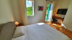 Een slaapkamer met een bed, een bureau, een stoel, een televisie en een raam met uitzicht op groen.