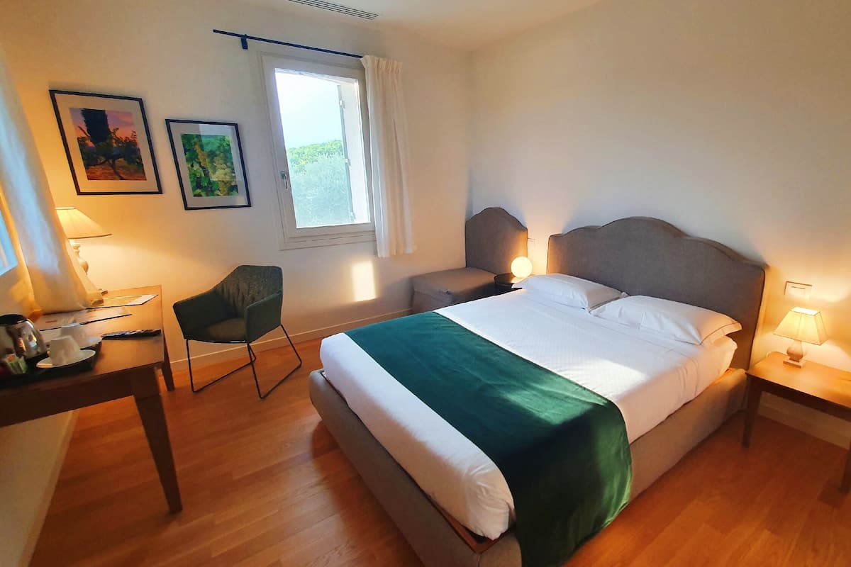 Een goed verlichte slaapkamer met een groot bed, een bureau, een stoel en twee bedlampjes.