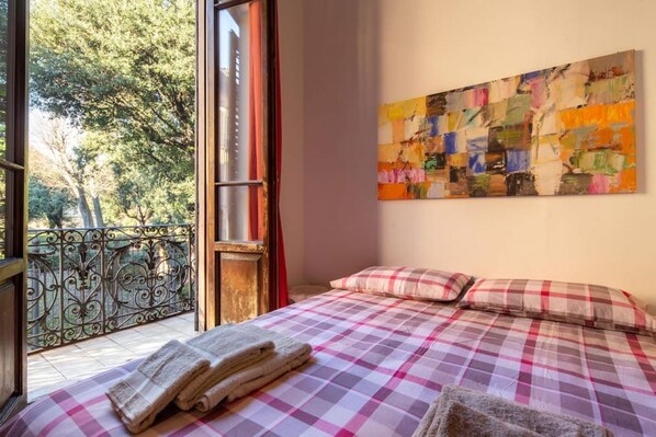Une chambre à coucher avec une couvre-lit à carreaux, un tableau accroché au mur et un balcon doté d’une balustrade en fer forgé.