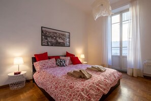 Une chambre à coucher avec un lit, deux lampes de chevet, un tableau encadré au mur et une fenêtre avec des rideaux.