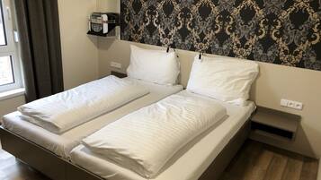 A double bed with white linens, a wall-mounted record player, and a patterned wallpaper.