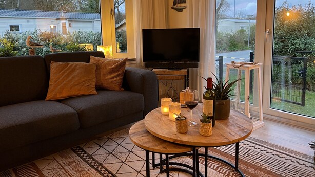A cozy living room with a sofa, a TV, a coffee table with candles, and a view of the outside.