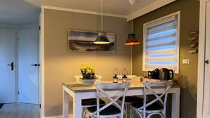 A dining area with a white table and chairs, a painting on the wall, and a window with blinds.