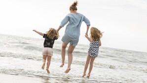A person jumping into the ocean with two children.
