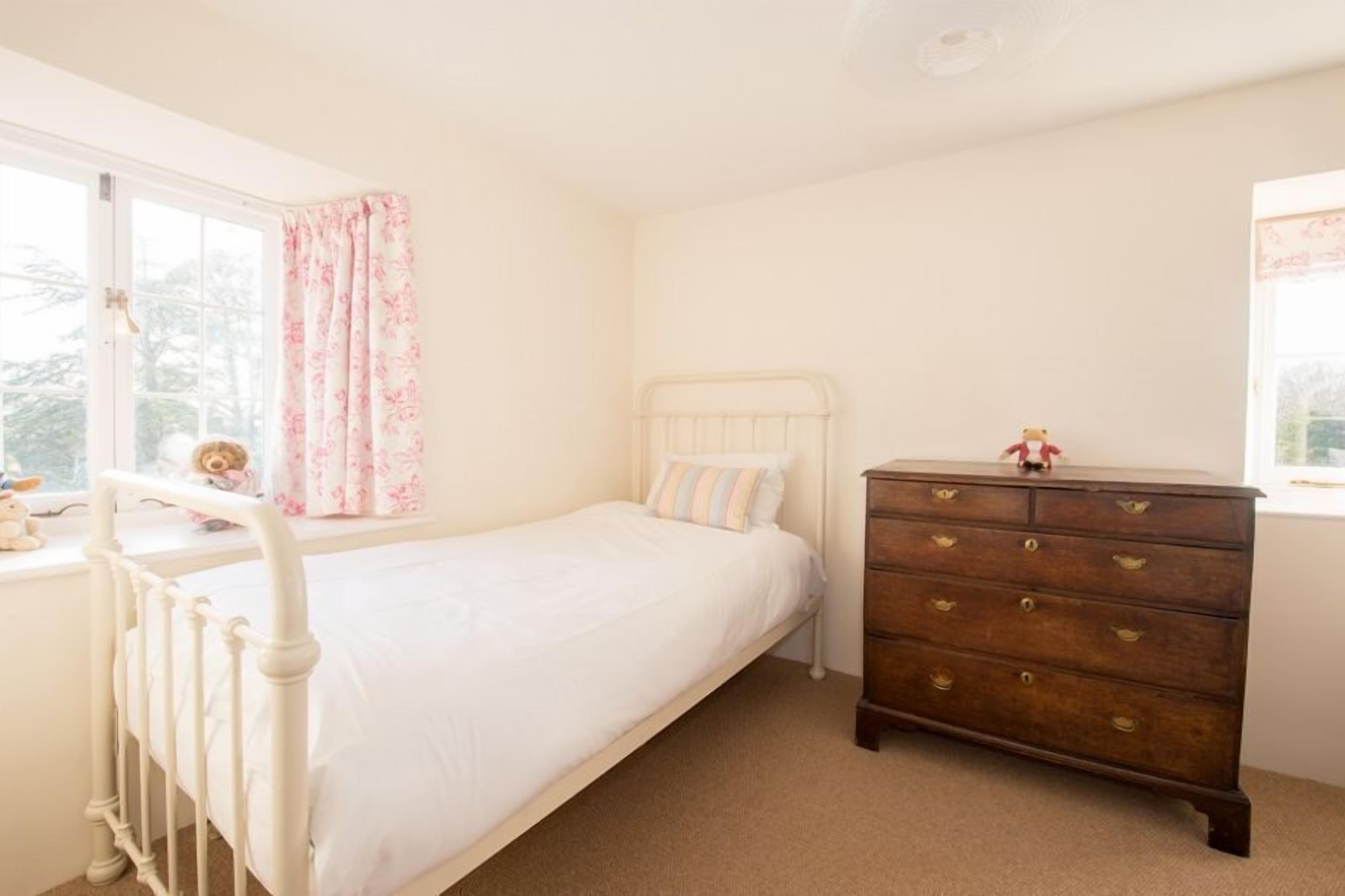 A bedroom with a single bed, a wooden dresser, and a window with curtains.