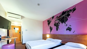 Habitación de hotel con dos camas, un escritorio, una silla, un televisor y un mapa mundial en la pared.
