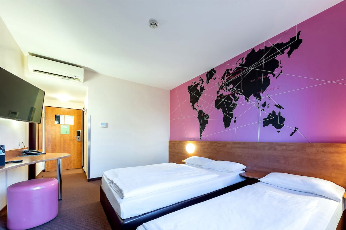 Habitación de hotel con dos camas, un escritorio, una silla, un televisor y un mapa mundial en la pared.