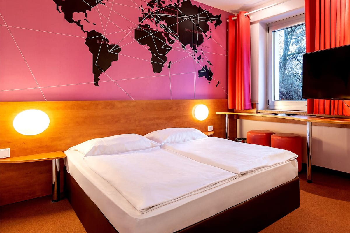 Habitación de hotel con una cama grande, dos mesitas de noche, un escritorio con silla, un televisor y una ventana con cortinas.
