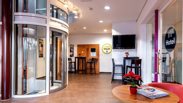 Un vestíbulo de hotel con una recepción, una zona de comedor y un área de descanso con una mesa y sillas.
