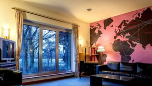 Una sala moderna con un amplio ventanal, un mural de mapa mundial, un sofá de cuero y un televisor.