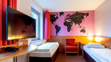 Habitación de hotel con cama, escritorio, computadora, silla y mapa mural.