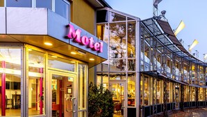 Un motel moderno con fachada de vidrio, un letrero de neón y una entrada adoquinada.