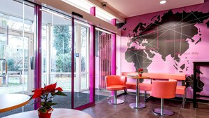 Un interior moderno con puertas de cristal que dan a un jardín, asientos en tonos rosa y naranja, y un mapa del mundo en la pared.