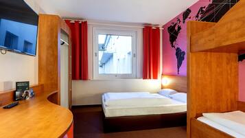Una habitación de hotel con cama, escritorio, televisión y ventana con cortinas.