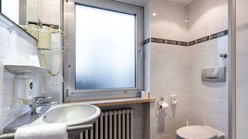 Un baño con ventana, lavabo, inodoro y radiador.