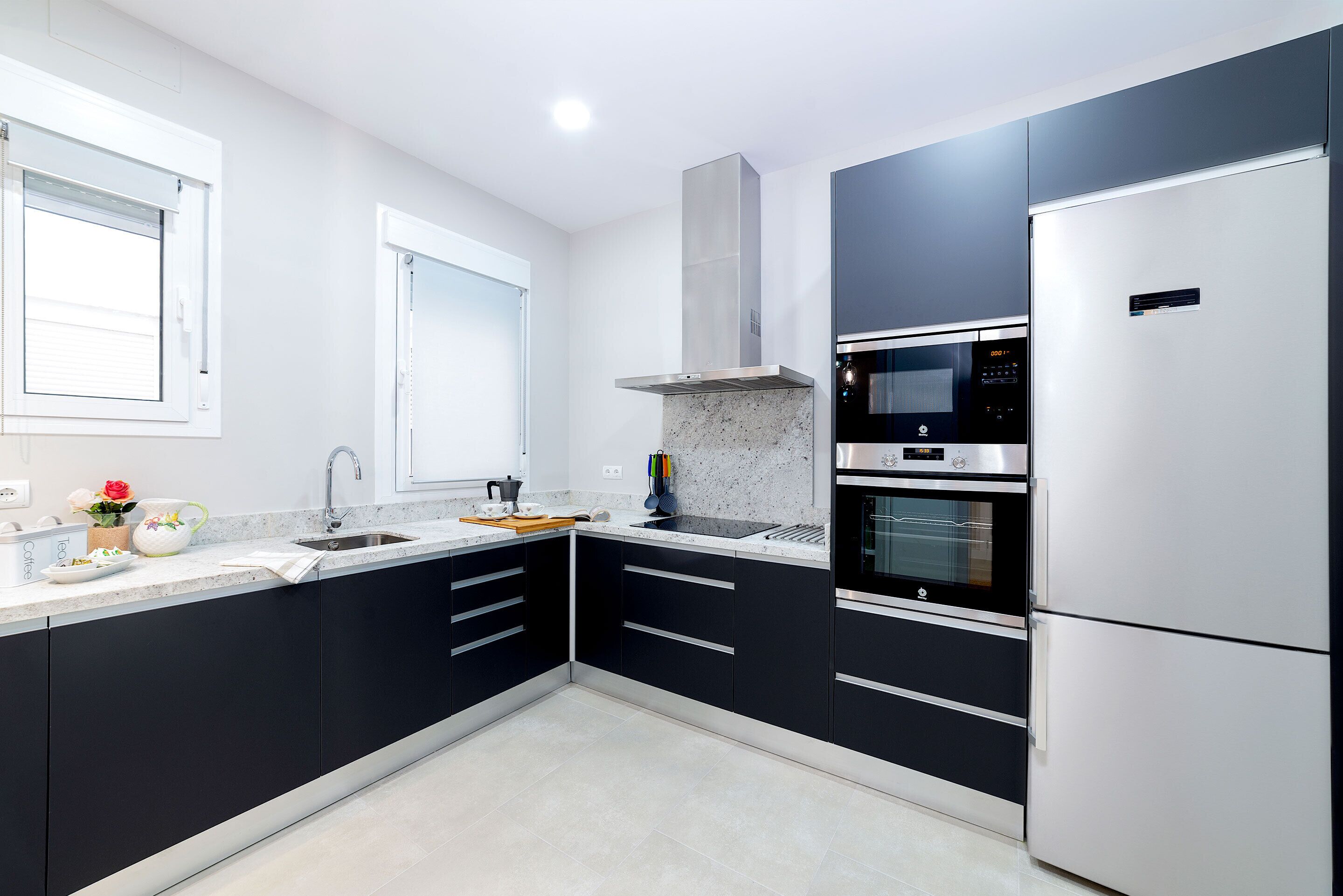 A modern kitchen with black cabinets, stainless steel appliances, and a window with blinds.