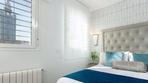 A bedroom with a large window, a radiator, a bed with a blue and white bedspread, and a wall-mounted light fixture. - Genteel Home Mateos Gago V (Seville)
