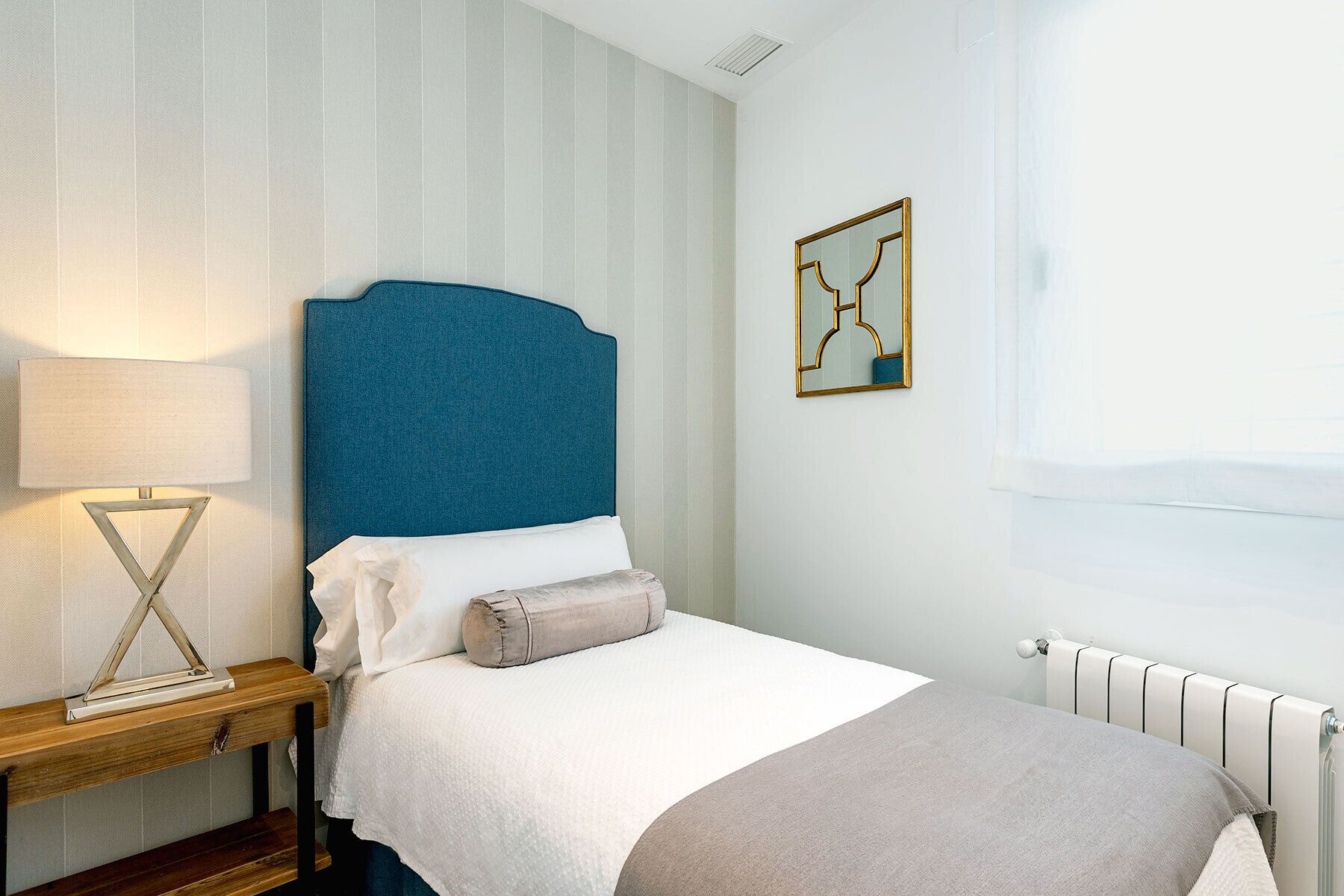 Una cama bien hecha con un cabecero azul, una lámpara de noche y una obra de arte abstracta enmarcada en la pared.