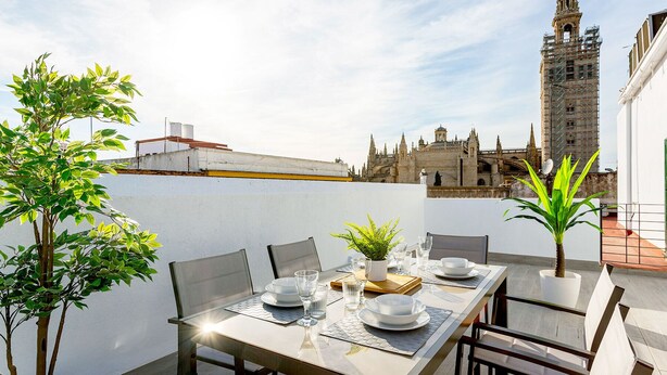 An outdoor dining area with a table set for four, surrounded by chairs, a potted plant, and a view of a historic building in the background. - Genteel Home Mateos Gago V (Seville)