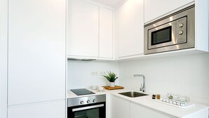 A compact kitchen with white cabinetry, a built-in microwave, a stove, and a sink. - Genteel Home Mateos Gago V (Seville)