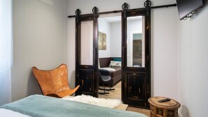A bedroom with a bed, a leather chair, a small round table with a remote, and a sliding door leading to another room. - Affittacamere I Canneggiatori (Abbadia San Salvatore)