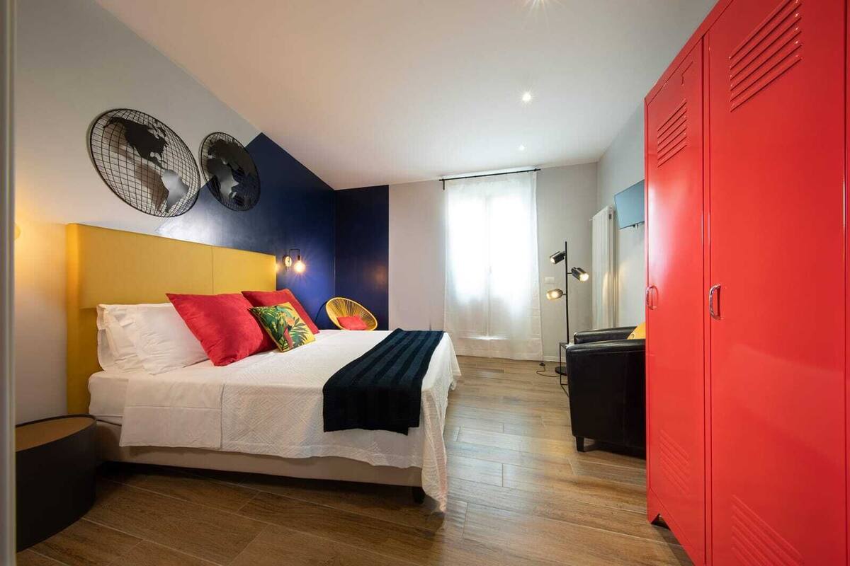 A bedroom with a bed, a red wardrobe, and a wall-mounted fan.