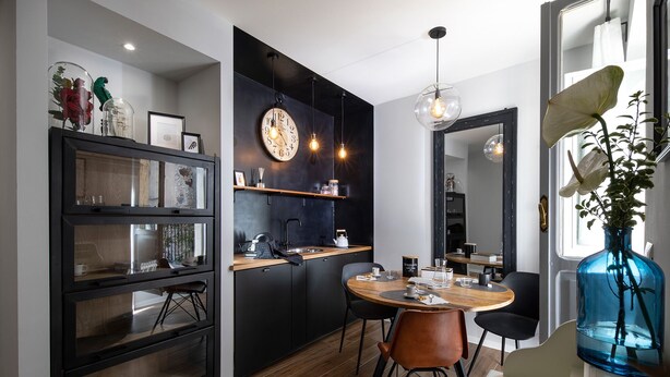A modern kitchen with a round dining table, black cabinetry, and a large clock on the wall. - Affittacamere I Canneggiatori (Abbadia San Salvatore)