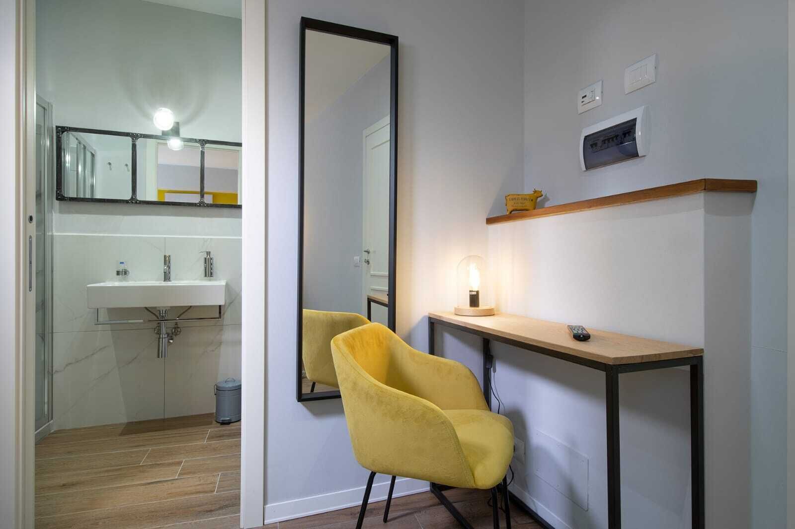 Un baño moderno con espejo, lavamanos y una silla amarilla.