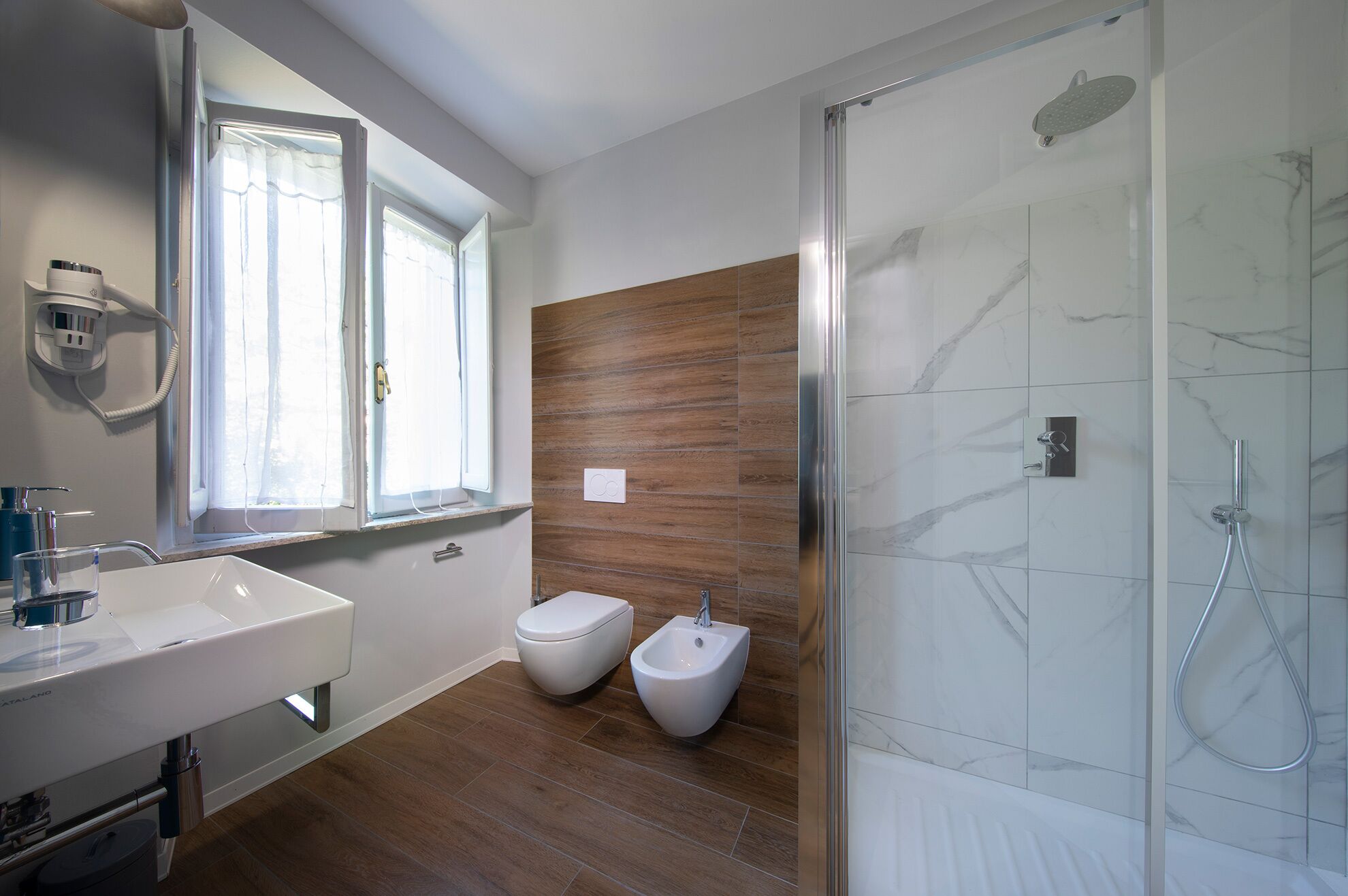 A modern bathroom with a large mirror, two bidets, a shower, and a sink.