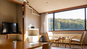 Une chambre moderne dotée d’un téléviseur à écran plat, d’une table à manger en bois, de chaises, d’un petit coin cuisine et d’une grande fenêtre donnant sur une forêt.