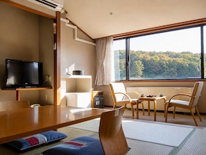 Une chambre moderne dotée d’un téléviseur à écran plat, d’une table à manger en bois, de chaises, d’un petit coin cuisine et d’une grande fenêtre donnant sur une forêt.