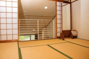 Um quarto japonês tradicional, com piso de tatame, biombos de shoji e vista para uma paisagem verde.