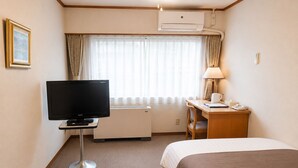 Une chambre d’hôtel équipée d’un lit, d’un bureau avec une lampe, d’une télévision et d’un appareil de climatisation.