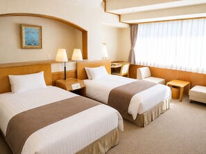 Une chambre d’hôtel avec deux lits, un bureau, une chaise et une fenêtre avec des rideaux.