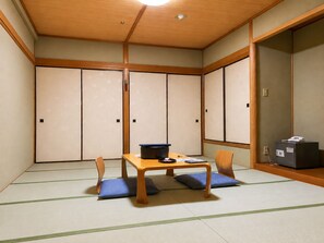 Ein traditioneller japanischer Raum mit Tatami-Boden, einem niedrigen Holztisch mit Kissen und verschiebbaren Shoji-Türen.