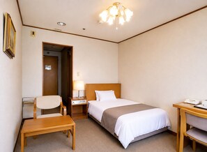 Une chambre d’hôtel comprenant un lit, une table de chevet, une chaise, un bureau, une lampe et une porte donnant sur une autre pièce.