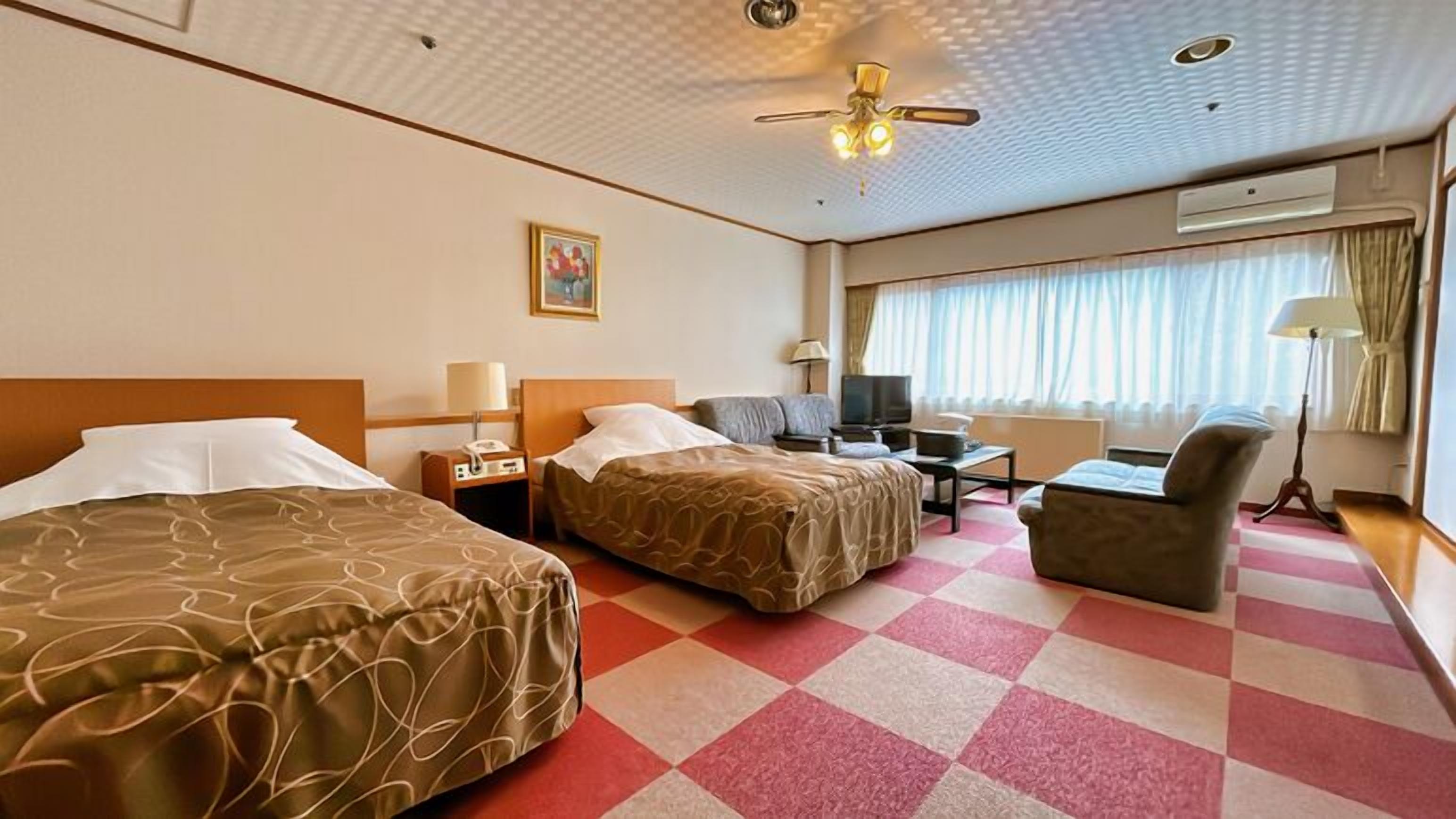 Una habitación de hotel con dos camas, un escritorio, una silla, un televisor y un ventilador de techo.