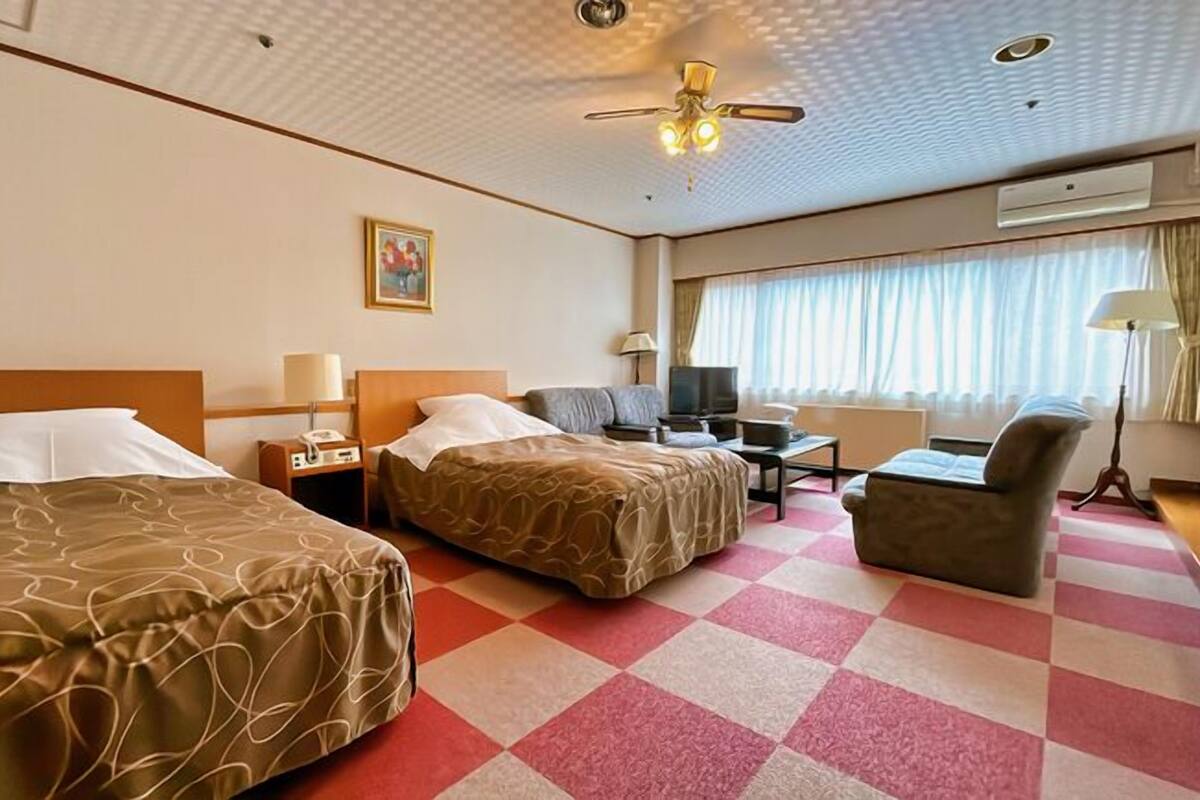 Una habitación de hotel con dos camas, un escritorio, una silla, un televisor y un ventilador de techo.