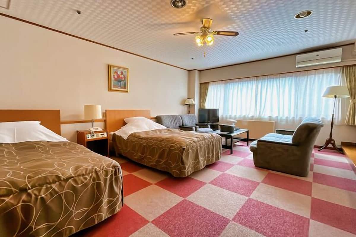 A hotel room with two beds, a desk, a chair, a television, and a ceiling fan.