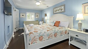 A bedroom with a bed, a nightstand, a ceiling fan, and a window with shutters. - Beachwalker Apartment:  Duplex within 100 steps to the sand. (Holmes Beach)